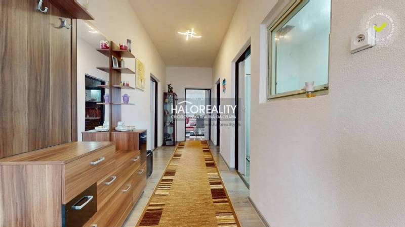 Interiér rodinného domu s dlouhou chodbou, podlahou s dřevěným dekorem a dřevěným nábytkem.