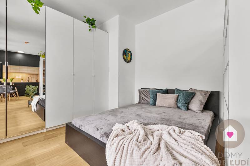 Ložnice v garsonce s postelí, bílou skříní a podlahou s dřevěným dekorem.