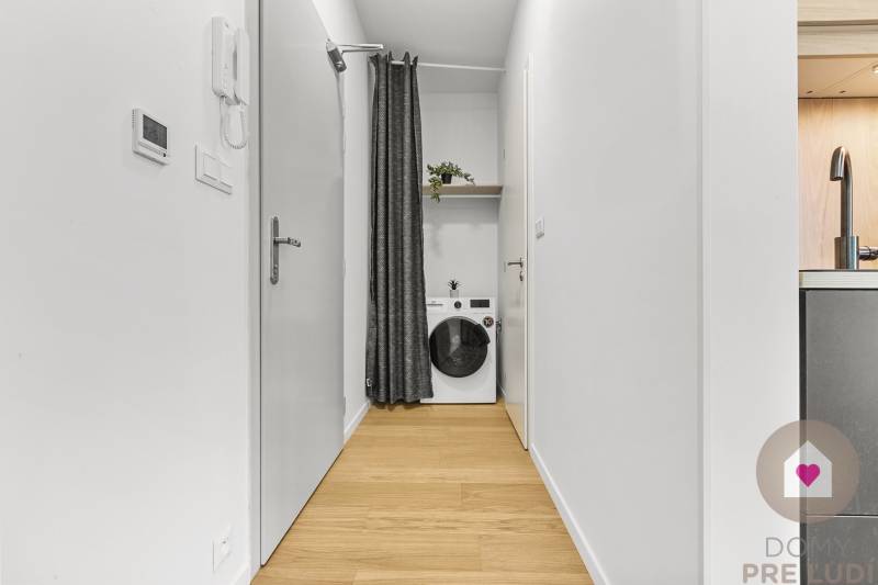 Úzká chodba v 1-pokojovém bytě se závěsem a pračkou.