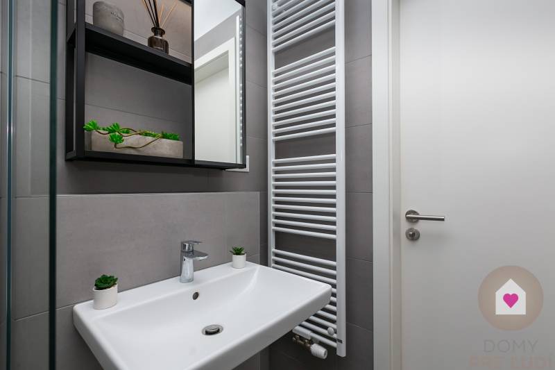 Koupelna v 1-pokojovém bytě s umyvadlem, žebříkovým radiátorem a úložnými policemi.