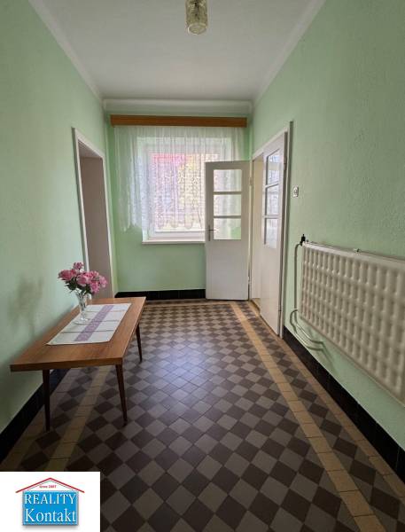 Chodba v rodinném domě s květinami na stole a kachličkovou podlahou.