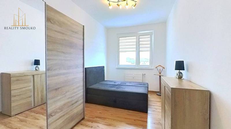 Světlá ložnice v 3pokojovém bytě s podlahou s dřevěným dekorem a velkou skříní.