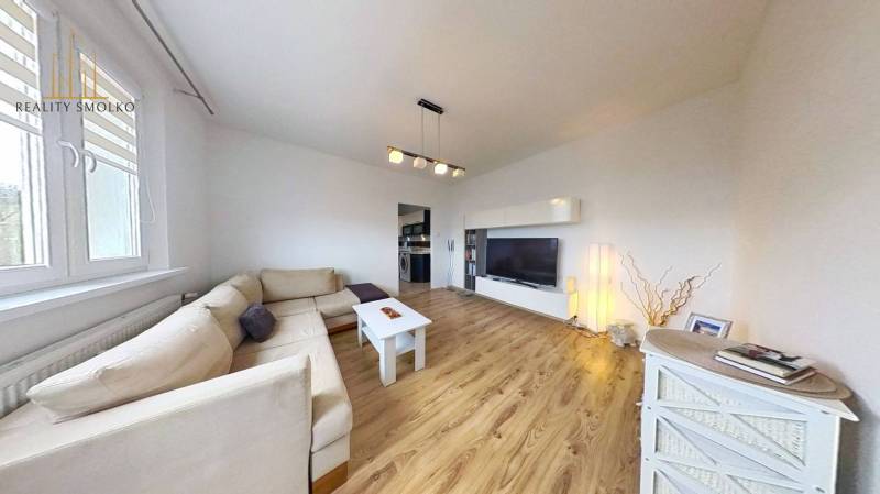 Obývací pokoj s podlahou s dřevěným dekorem v 3-pokojovém bytě se světlou sedačkou a TV skříňkou.