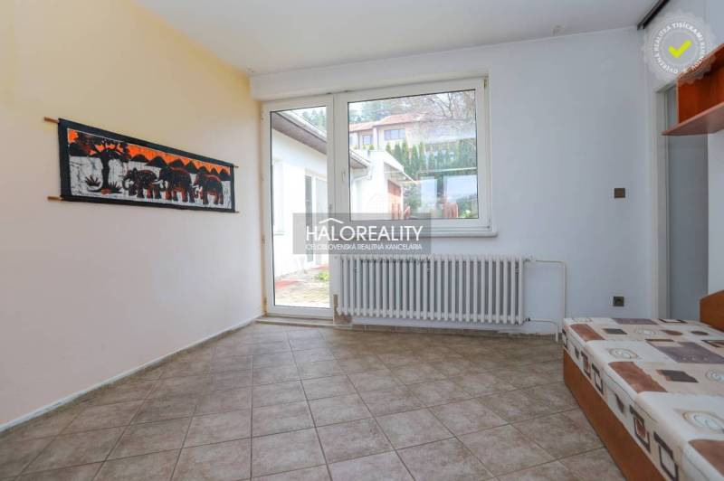 Interiér rodinného domu s dlaždicovou podlahou, sedačkou a velkým oknem.