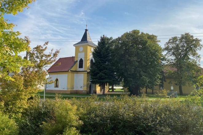 Kostel obklopený zelení v Práznovcích na zemědělských a lesních pozemcích.