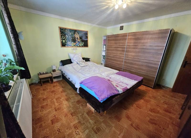 Ložnice v rodinném domě s postelí, skříní a podlahou s dřevěným dekorem.