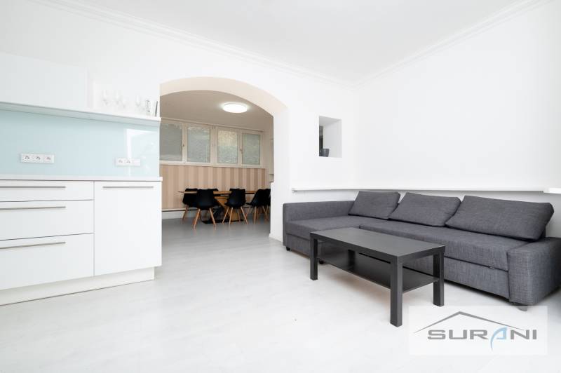 Obývací pokoj čtyřpokojového bytu s kuchyňským koutem a sedací soupravou.