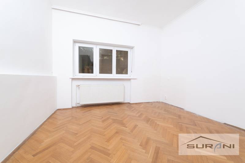 Pokoj ve 4pokojovém bytě s bílými stěnami a podlahou s dřevěným dekorem.