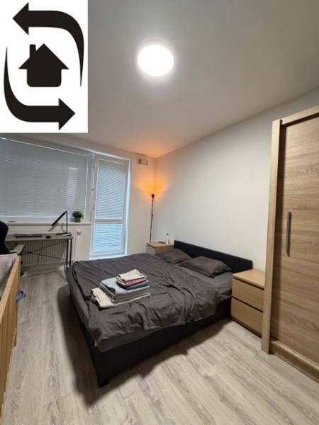 Ložnice v dvoupokojovém bytě s podlahou s dřevěným dekorem a postelí vedle okna.