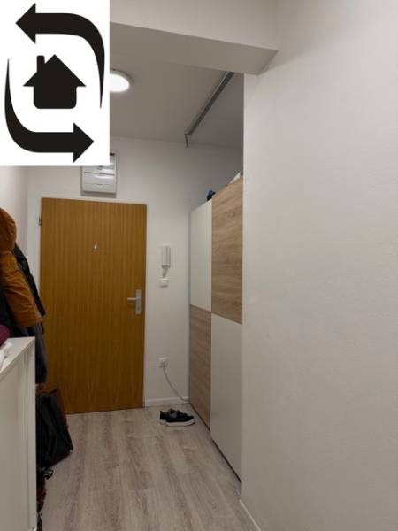 Vstupní chodba v 2-pokojovém bytě, bílé stěny a dveře, podlaha s dřevěným dekorem.