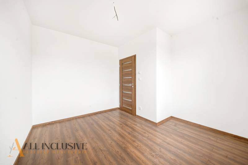 Prázdný pokoj v rodinném domě s bílými stěnami a podlahou s dřevěným dekorem.