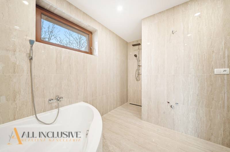 Koupelna v rodinném domě s vanou a sprchou, stěny mají mramorový vzhled.