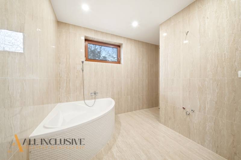 Koupelna s vanou a dlažbou v rodinném domě. Přírodní tóny a stylové osvětlení.