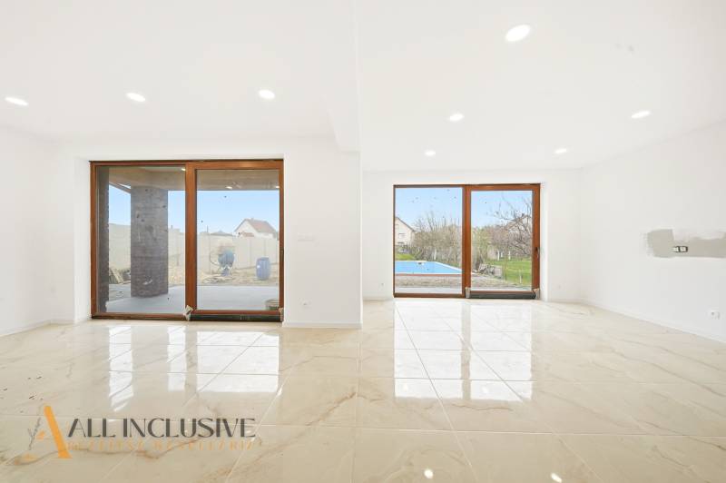 Obývací pokoj v rodinném domě s velkými skleněnými dveřmi a výhledem na dvůr.