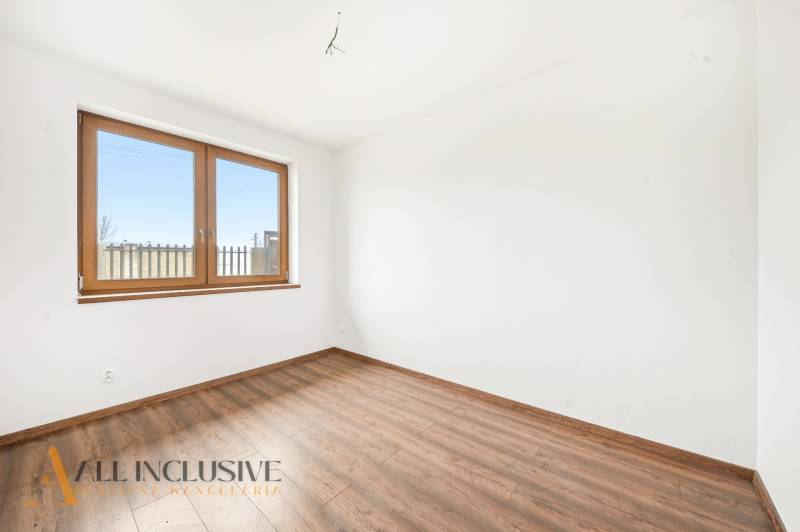 Pokoj v rodinném domě s bílými stěnami, dřevěným oknem a podlahou s dřevěným dekorem.