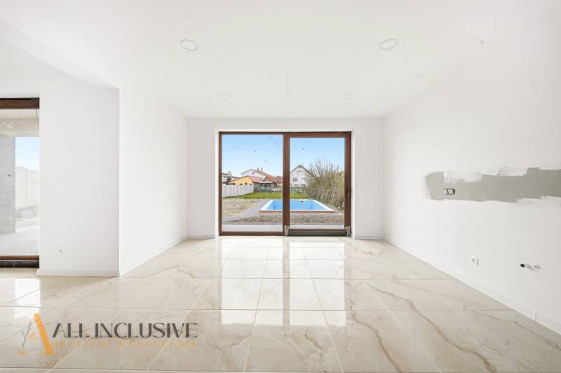 Interiér rodinného domu s velkými okny a výhledem na dvůr s bazénem.