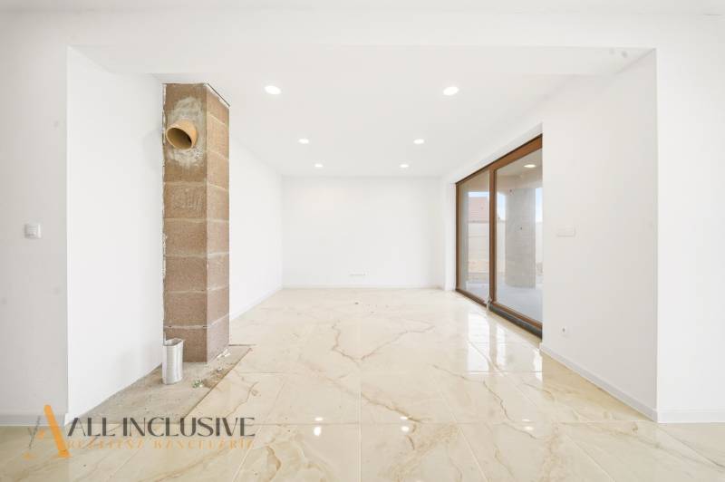 Prostorná místnost rodinného domu s velkými okny a světlou podlahou.