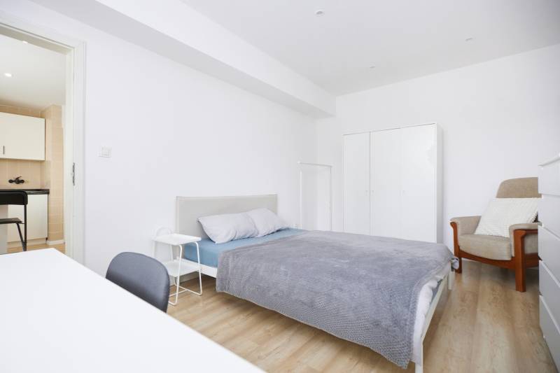 Ložnice dvoupokojového bytu s postelí, skříní a podlahou s dřevěným dekorem.