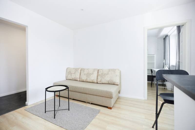 Obývací prostor s pohovkou, stolkem a podlahou s dřevěným dekorem v 2pokojovém bytě.