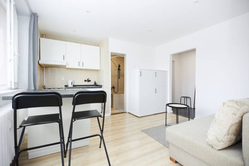 Interiér 2-pokojového bytu s kuchyní, barovými stoličkami a podlahou s dřevěným dekorem.