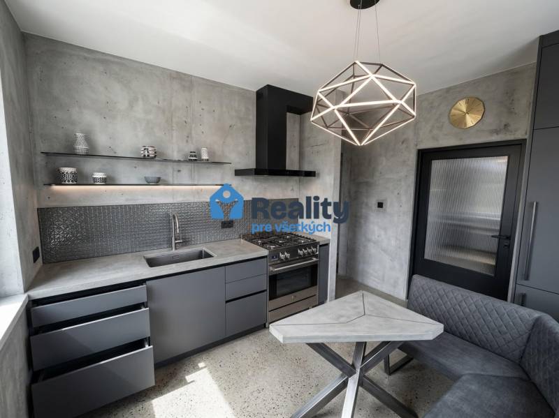 Kuchyně v 2-pokojovém bytě s betonovým vzhledem a geometrickým svítidlem.