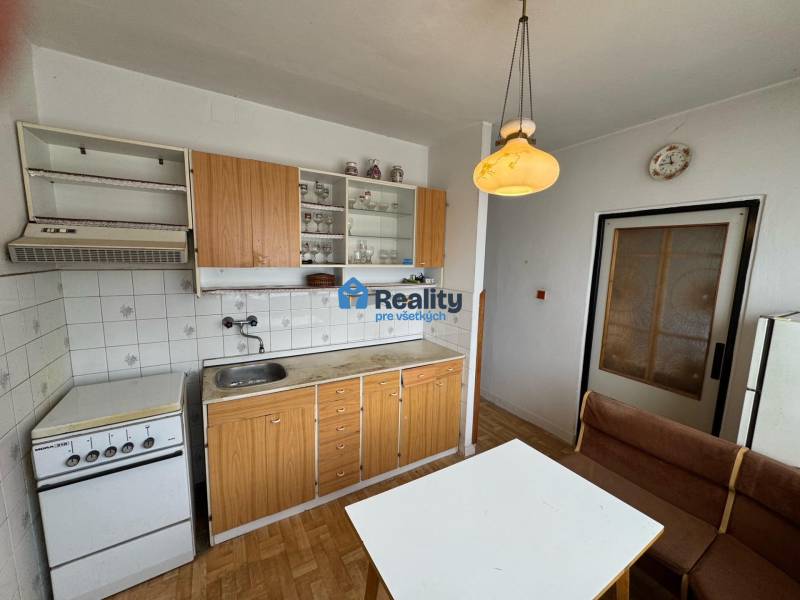 Kuchyně v 2-pokojovém bytě s kuchyňskou linkou, stolem, lavicí a podlahou s dřevěným dekorem.