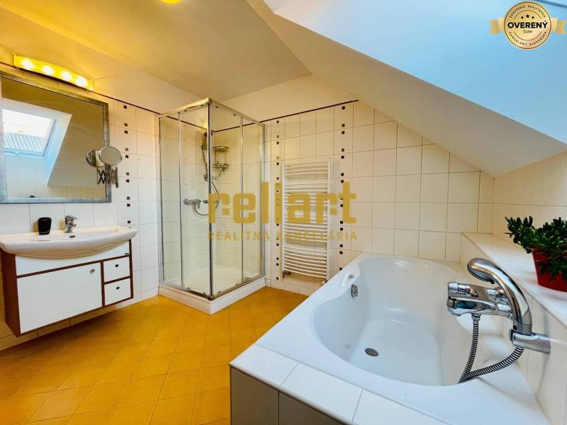 Koupelna v rodinném domě s vanou, sprchovým koutem a šikmým stropem.