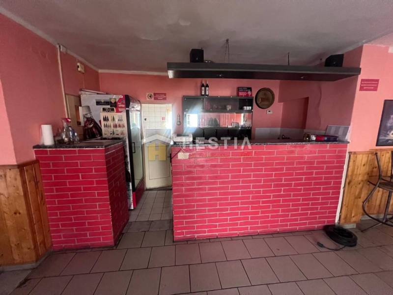 Gastro prostory s cihlovým barem, podlaha s dřevěným dekorem, stěny s růžovým nátěrem.