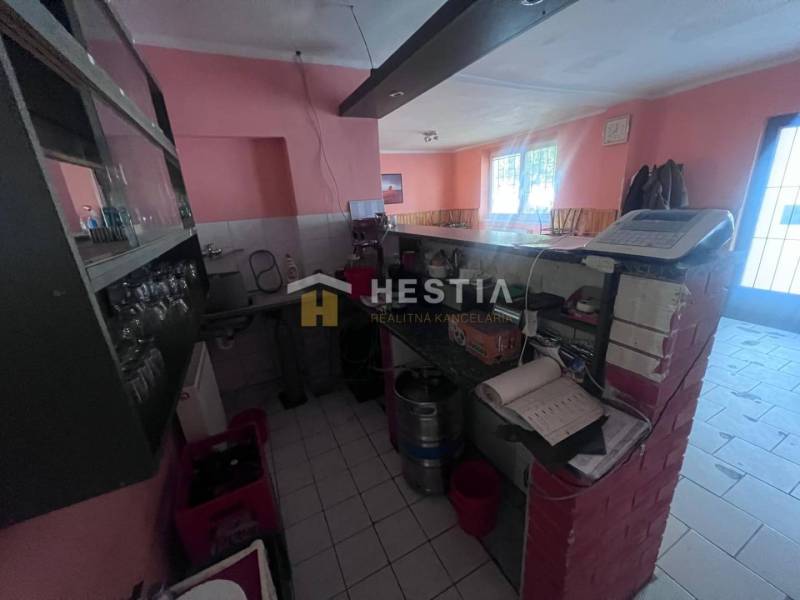 Interiér gastro prostorů s barovým pultem, pokladnou a sklenicemi na poličce.