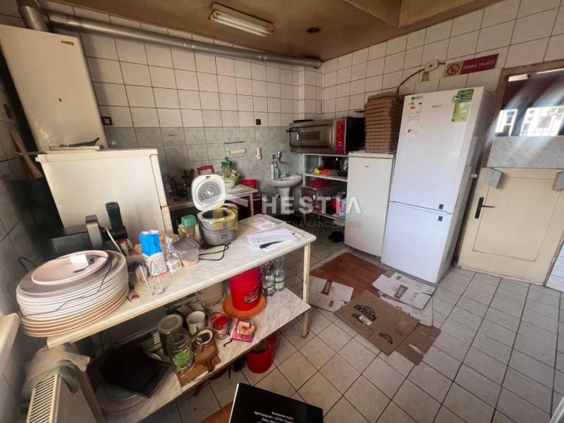 Kuchyně s gastro prostory, bílá dlažba, zásobníky, kuchyňské potřeby, ventilátor, ledničky.