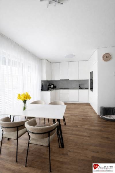 Jídelní stůl se židlemi a kuchyň v 3-pokojovém bytě s podlahou s dřevěným dekorem.