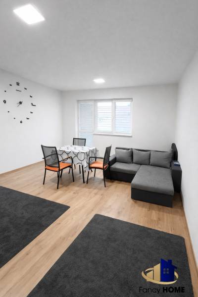 Obývací pokoj v 2-pokojovém bytě s pohovkou, stolem a podlahou s dřevěným dekorem.