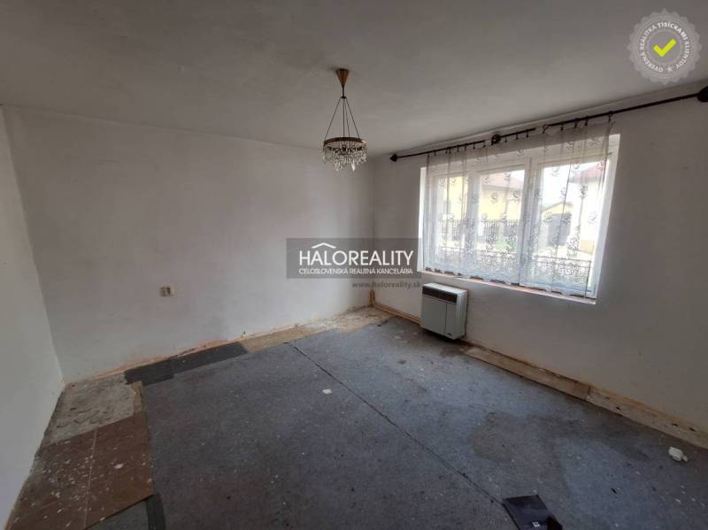 Pokoj s kobercem, bílými stěnami a velkým oknem, vhodný k rekonstrukci; Pozemky - bydlení.