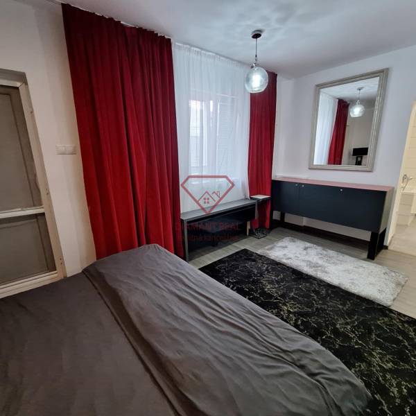 Interiér rodinného domu s červenými závěsy, zrcadlem a tmavým kobercem.