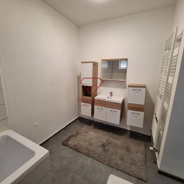 Koupelna v rodinném domě s bílým nábytkem a tmavou dlažbou.