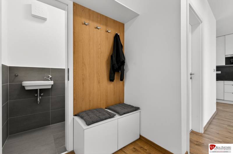 Předsíň v 2-pokojovém bytě s lavičkou, věšáky a umyvadlem, podlaha s dřevěným dekorem.