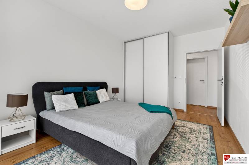 Ložnice v 2-pokojovém bytě s postelí, nočním stolkem a skříní.