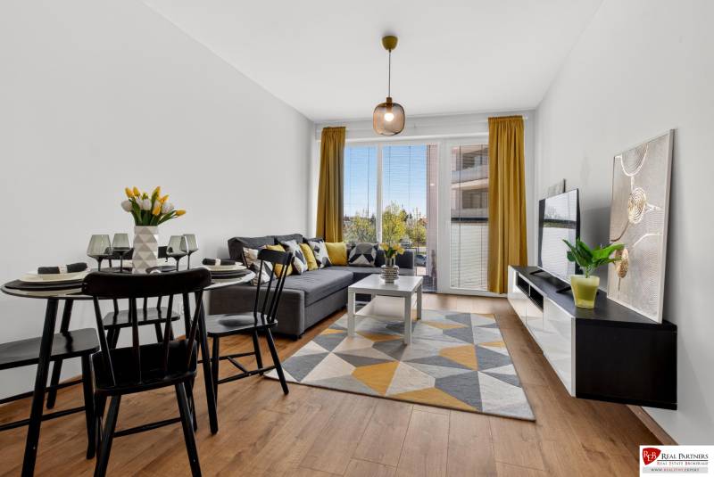 Obývací pokoj v 2-pokojovém bytě s podlahou s dřevěným dekorem, pohovkou a jídelním stolem.