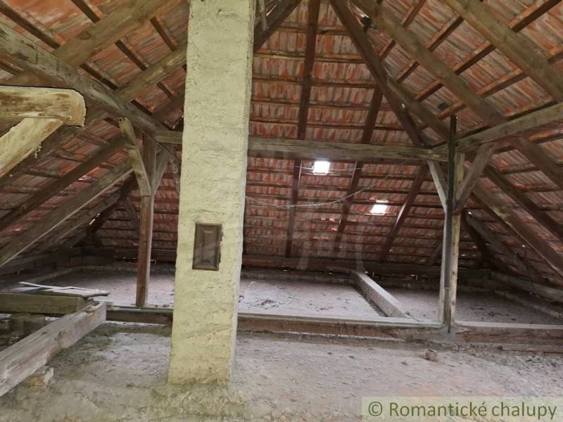 Podkroví v rodinném domě s dřevěnými trámy a cihlovou střechou.