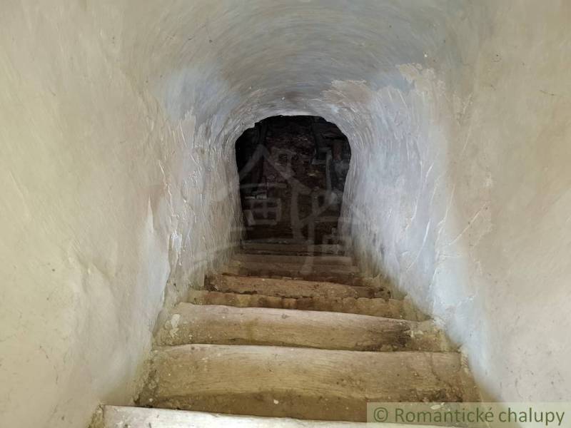 Kamenné schody vedoucí do sklepa v rodinném domě, zdi s hrubou omítkou.