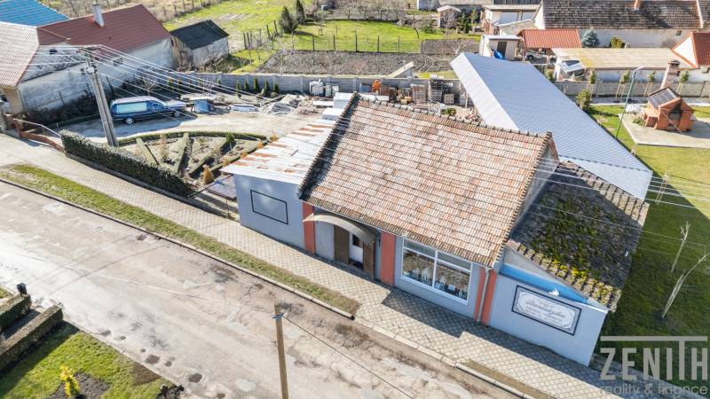 Obchodní prostory v Okoči s tradiční střechou, chodníkem a zahradou.