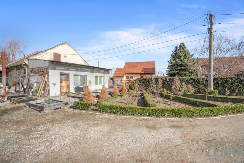 Obchodní prostory v Okoči s úpravou zahrady, obklopené stromy a keři.