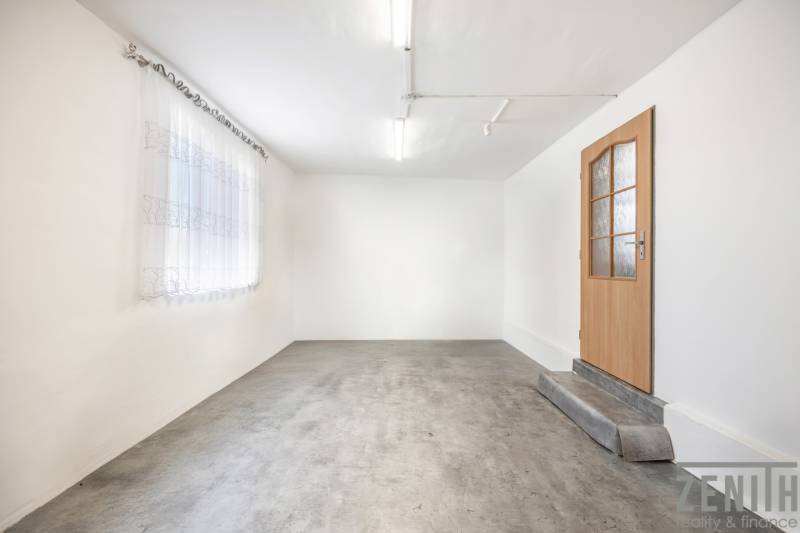 Bílé stěny, betonová podlaha, dřevěné dveře a záclona v obchodních prostorách.