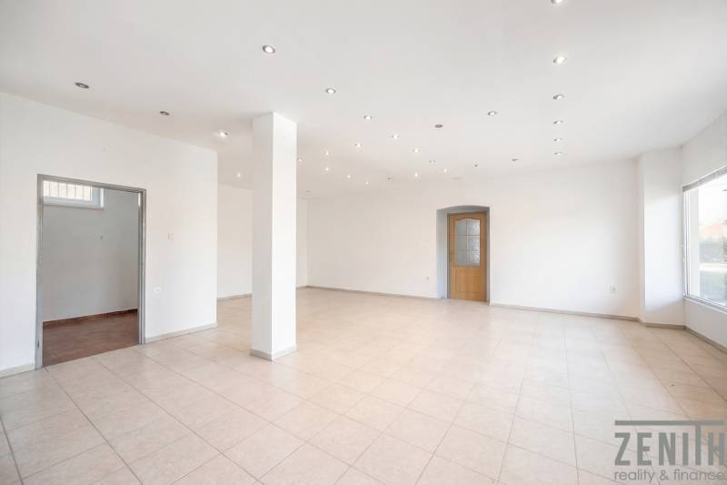 Prostorné obchodní prostory s bílými stěnami, dlažbou a rozsvícenými stropními světly.