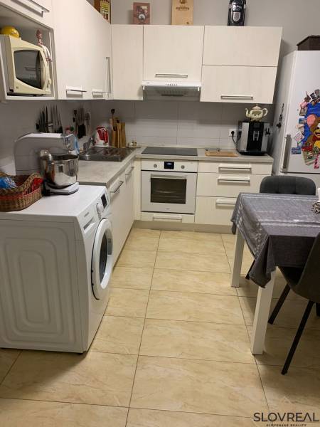 Kuchyně ve 2-pokojovém bytě s bílými skříňkami a keramickou podlahou.