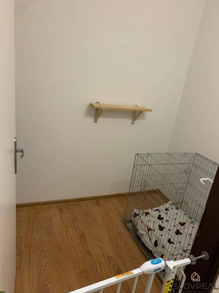 Malá místnost s nástěnnou policí, podlahou s dřevěným dekorem a klecí pro zvíře.