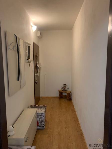 Úzká předsíň s bílými stěnami, podlaha s dřevěným dekorem a minimalistickým nábytkem.