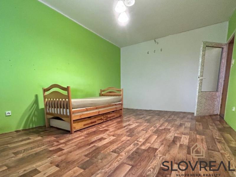 Pokoj s postelí v 2pokojovém bytě, podlaha s dřevěným dekorem, zelené stěny.