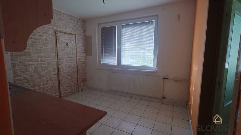 Pokoj s dlažbou, velkým oknem a radiátorem v 2-pokojovém bytě.