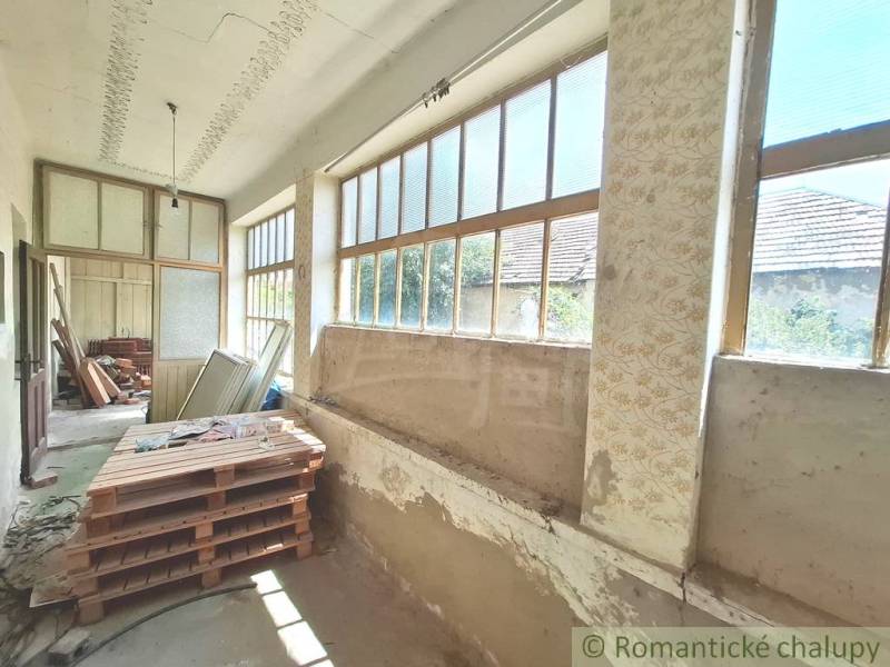 Chata s prostornou verandou, velkými okny a rozmanitým uskladněným materiálem.